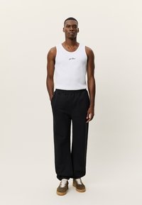 Λευκό αμάνικο τοπ με μικρό μαύρο λογότυπο, συνδυασμένο με φαρδιά μαλακά μαύρα παντελόνια. Το υπόδημα έχει καφέ και λευκές λεπτομέρειες.