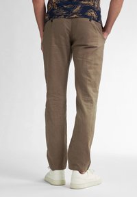 Pantaloni in lino beige con una vestibilità rilassata, caratterizzati da una leggera texture e un design a gamba dritta, abbinati a sneakers bianche.