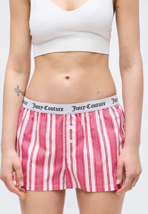 Torace feminin îmbrăcat într-un crop top alb și pantaloni scurți Juicy Couture cu dungi roșii și albe, detalii cu nasturi și logo pe talie.