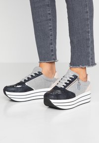 Gray and navy sneakers with a shiny texture, padded tongue, and a side zipper. Features white striped platform sole and soft pink accents.