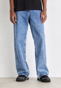 Ljusblå denimjeans med lös passform, med en klassisk femficksdesign och en lätt tvätt. Bärs med svarta skor.