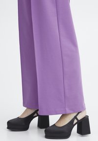 Pantalons larges violets en tissu lisse, associés à des talons plateformes noirs avec un bout rond et une bride arrière, mettant en valeur une couleur contrastante.