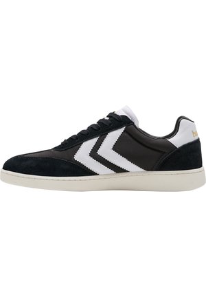 Black and white sneakers featuring a suede and synthetic upper with a low-top design, contrasting chevron stripes, and a rubber sole.