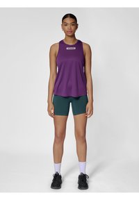Fioletowa bezrękawnik sportowy z logo, zestawiony z zielonymi szortami. Noszony z czarnymi butami sportowymi i białymi skarpetami, charakteryzującymi się gładką teksturą.