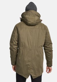 Oliven grøn parka jakke, quiltet tekstur, hætte med justerbare snore, designet med en længere ryg og trykknapper i kanten.