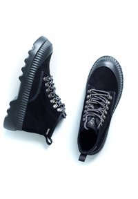 Mustad mustad ankle' boots, mille paisid kummist tallad, metallist silmad ja hall nööridetailed. Omab ümmargust varvast ja kandetaili.