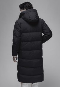 Sort pufferjakke med en oversized hætte, der har en lang silhuet og quiltet struktur. Glat stof med betydelig polstring for varme.