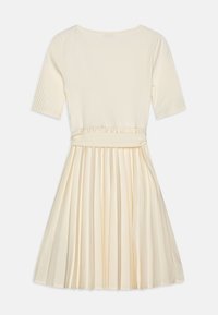 Polven mittainen mekko, jossa on resoroitu kermanvärinen yläosa ja laskostettu satiinihame. Yläosassa on lyhyet hihat ja kerätty vyötärönauha.