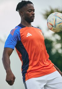 Camisa desportiva Adidas nas cores laranja, azul e marinho. Mangas curtas e decote redondo, com um design em gradiente e o logotipo da marca.