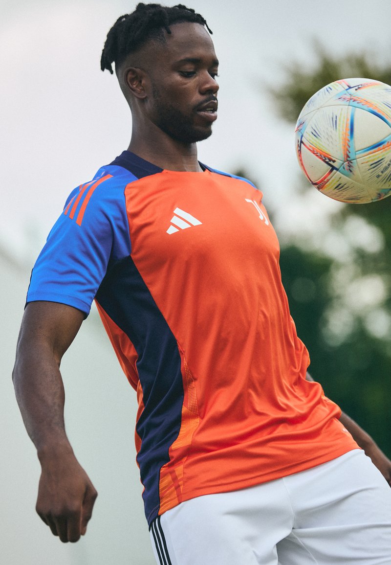 Camisa desportiva Adidas nas cores laranja, azul e marinho. Mangas curtas e decote redondo, com um design em gradiente e o logotipo da marca.