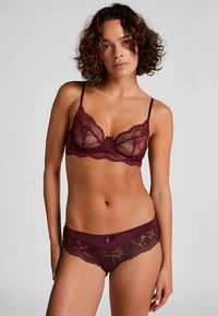 Bordeauxkleurige kanten lingerie set met delicate bloemmotieven, doorschijnende cups, verstelbare bandjes en een bijpassende slip met een klein strikje als accent.