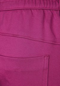 Fuchsiová tkanina se hladkým povrchem, která má boční kapsu a elastický pas. Čisté švy podél okrajů, minimalistický design.