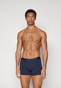 Marineblaue Baumwollboxershorts mit glattem Stoff und kontrastierendem Satinhüftbund, getragen von einem Modell mit muskulösem Körperbau.