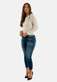 Cardigan bianco a fantasia con colletto rotondo, chiusura con bottoni, abbinato a jeans skinny blu scuro e scarpe con tacco nere.