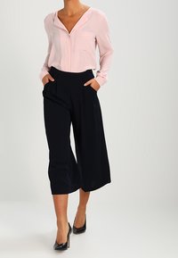 Blusa rosa chiaro con scollatura a V e taschino sul petto, abbinata a pantaloni a gamba larga blu navy e tacchi neri. Tessuto morbido con una vestibilità comoda.