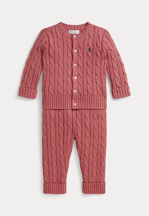 Kindergröße rosa Strickjacke mit weißen Knöpfen und passenden Hosen mit gekrempelten Bündchen an den Knöcheln auf weißem Hintergrund.
