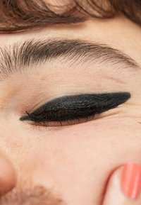 Närbild av ett öga med svart eyeliner applicerat i en vingeform. Hudtonen är ljus med subtila texturer. Ögonfransarna är mörka och tydliga.