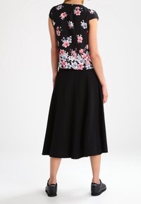 Blommönstrad svart topp med korta ärmar som matchas med en svart A-linjeformad kjol. Outfiten har en slät textur och en avslappnad design. Svarta sneakers fulländar looksen.