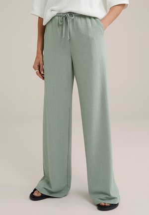 Lichtgroene, textuurvolle, wijde broek met een elastische tailleband en trekkoord. Gestyled met zwarte sandalen.
