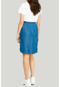 Jeansskørt i mellemblå, knælængde, med elastisk talje og buet kant. Sat sammen med hvide sneakers og en hvid t-shirt.