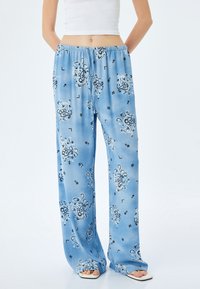 Pantalons larges bleu clair en tissu lisse, ornés de motifs floraux noirs et dotés d'une taille élastique pour plus de confort.