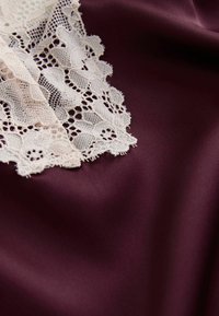 Țesătură burgundă cu o margine delicată din dantelă albă. Dantela prezintă modele florale și margini ondulate, creând un contrast texturat.