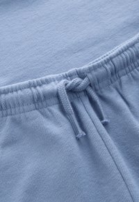 Světle modrá tkanina zblízka ukazující elastický pás s uvázaným tkaničkovým šňůrkou na měkkém texturovaném oděvu.
