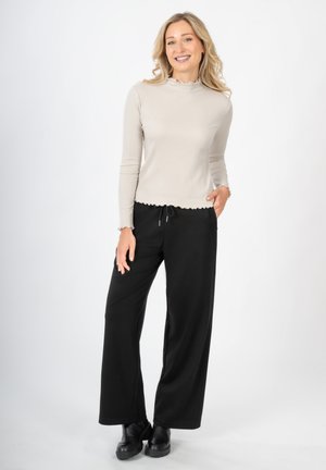 Beige geribbelde lange mouw top met een geschulpte halslijn, gecombineerd met zwarte wijde broek en zwarte enkellaarzen, op een neutrale achtergrond.