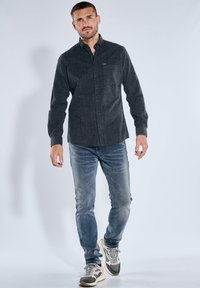 Dunkelgrau gestreiftes Hemd mit Kragen, kombiniert mit verblassten blauen Jeans und Sneakers mit grauen und weißen Akzenten.