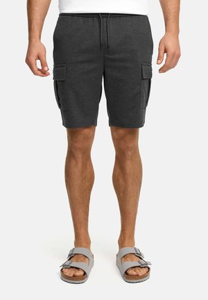 Mężczyzna ubrany w ciemnoszare szorty typu cargo z przednimi kieszeniami oraz szare sandały z klamrą, stojący na białym tle.