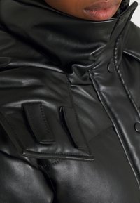 Chaqueta de cuero negra con un cuello alto, que presenta botones y detalles con solapas en los hombros. Textura suave y diseño elegante.