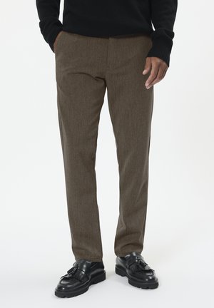 Braune, strukturierte Hose mit schmaler Passform. Kombiniert mit schwarzen Lederschuhen mit Quastenakzenten. Schlichtes, sauberes Design.