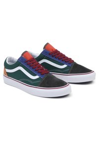 Een paar lage sneakers met een groene canvas, een zwarte suède neus, een blauw oogstikpaneel, een rode tong, kastanjebruine veters, een witte zijstreep en witte rubberen zolen.