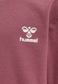 Maroonowy materiał odzieżowy z gładką teksturą. Posiada biały nadruk z logo stylizowanej pszczoły oraz słowo "hummel" poniżej.