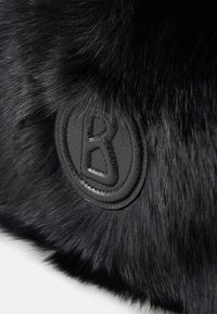 Sort håndtaske i imiteret pels med en struktureret overflade og en rund sort læderlap med et præget "B"-logo.