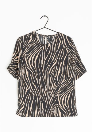 Blusa de manga corta con estampado de rayas de cebra negras y beige colgada en una percha negra sobre un fondo blanco.