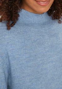 Maglione a collo alto di colore azzurro chiaro realizzato in morbido materiale a maglia, con colletto a coste e una texture liscia. Vista ravvicinata.