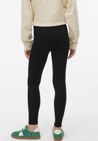 Leggings noirs en matériau extensible, design ajusté et taille haute, associés à des baskets vertes et blanches.