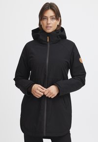 Black waterproof jacket with hood, front zipper, and two side pockets. Features a textured fabric and a brown leather logo patch on sleeve.