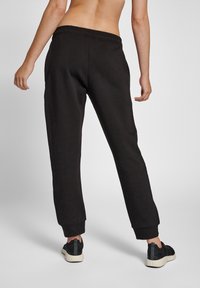 Pantalones jogger negros con cintura y puños elásticos, que presentan una textura suave. Combinados con zapatillas deportivas negras, mostrando un ajuste relajado.
