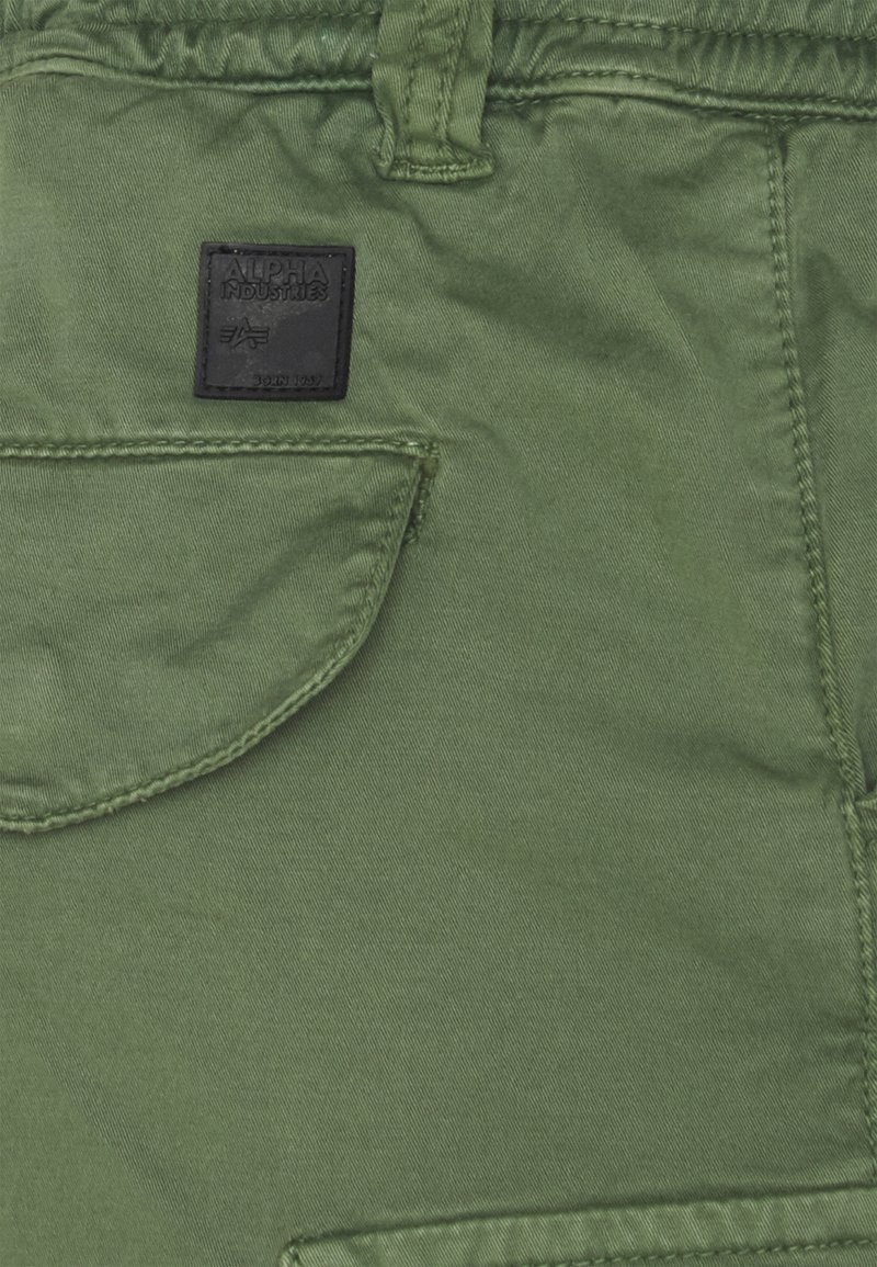 Olivenfarbene Stoff-Cargoshorts mit einer Vordertasche und einem schwarzen Etikett, gestickten Details und einer strukturierten Oberfläche.