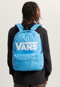 Světlomodrý batoh Vans s velkým bílým logem, polstrovanými nastavitelnými popruhy, jednou přední kapsou a texturovaným materiálem.