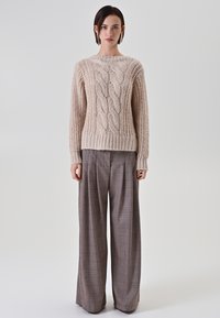 Maglione beige a trecce con scollo rotondo e orlo a coste, abbinato a pantaloni a gamba larga a quadri nei toni del marrone e crema.