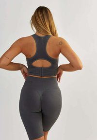 Szary stanik sportowy z wycięciem, regulowanymi ramiączkami i prążkowaną fakturą, w zestawieniu z pasującymi spodniami rowerowymi o wysokim stanie.