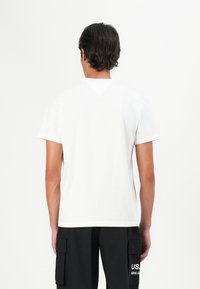 T-shirt en coton blanc à manches courtes, décolleté rond et un détail en triangle à l'arrière du cou. Associé à un short cargo noir.