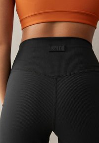 Mustad soonilised legginsid mustas värvuses, millel on kõrge vöökoht ja ristkülikukujuline must logotagi. Figuri löövad siluett rõhutab talje.