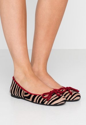 Bailarinas de tela a rayas en negro y beige, con un ribete rojo y lazos decorativos de cuerda roja en la puntera. Diseño de suela plana.