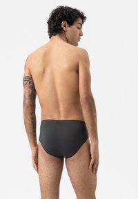 Grijze heren zwemslips met een elastische tailleband, gladde textuur en aansluitend ontwerp, getoond vanuit een zij-achterste hoek.