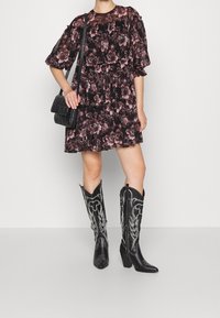 Robe fleurie noire avec manches bouffantes, design à niveaux ; associée à des bottes de cowboy en cuir noir avec des coutures argentées et des talons carrés.