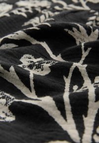 Tessuto nero con stampa botanica in bianco sporco. Il design include foglie e rami con un aspetto texturizzato.